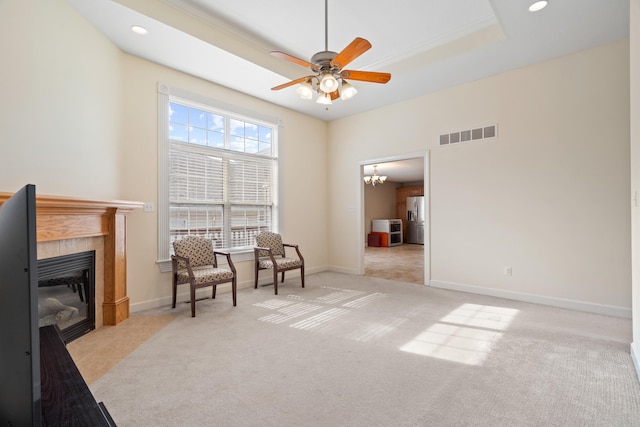 sitting room featuring ceiling fan with notable chandelier, a tray ceiling, a tiled fireplace, light colored carpet, and visible vents