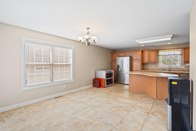 kitchen featuring a sink, stainless steel fridge, a chandelier, pendant lighting, and light countertops