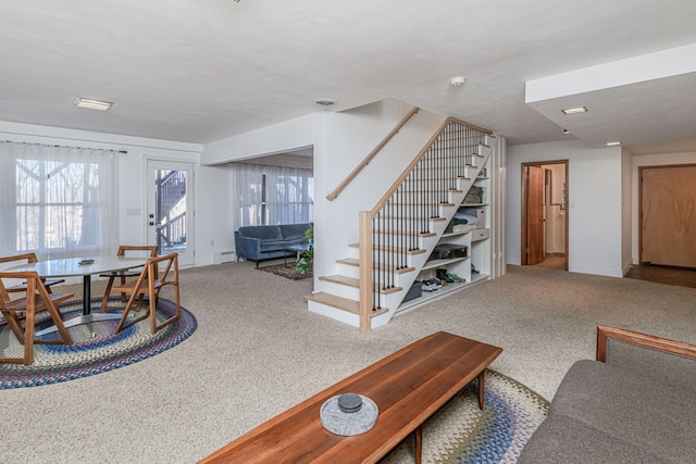 carpeted living room featuring baseboard heating, baseboards, a healthy amount of sunlight, and stairs