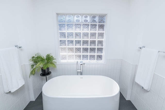 bathroom with tile patterned flooring, tile walls, a freestanding tub, and a wainscoted wall