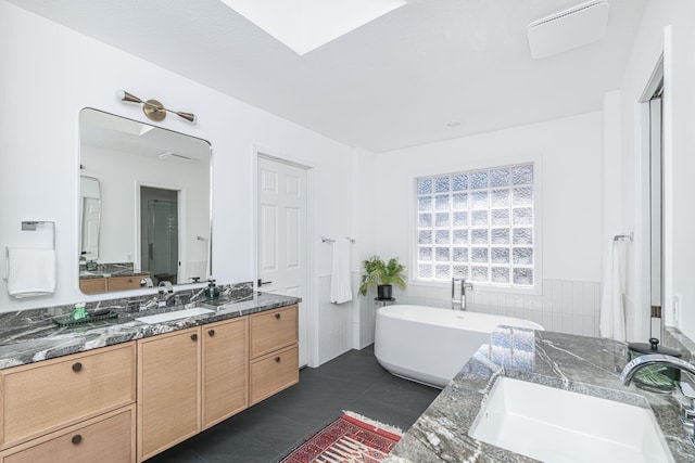 full bath with tile patterned floors, a wainscoted wall, vanity, tile walls, and a soaking tub