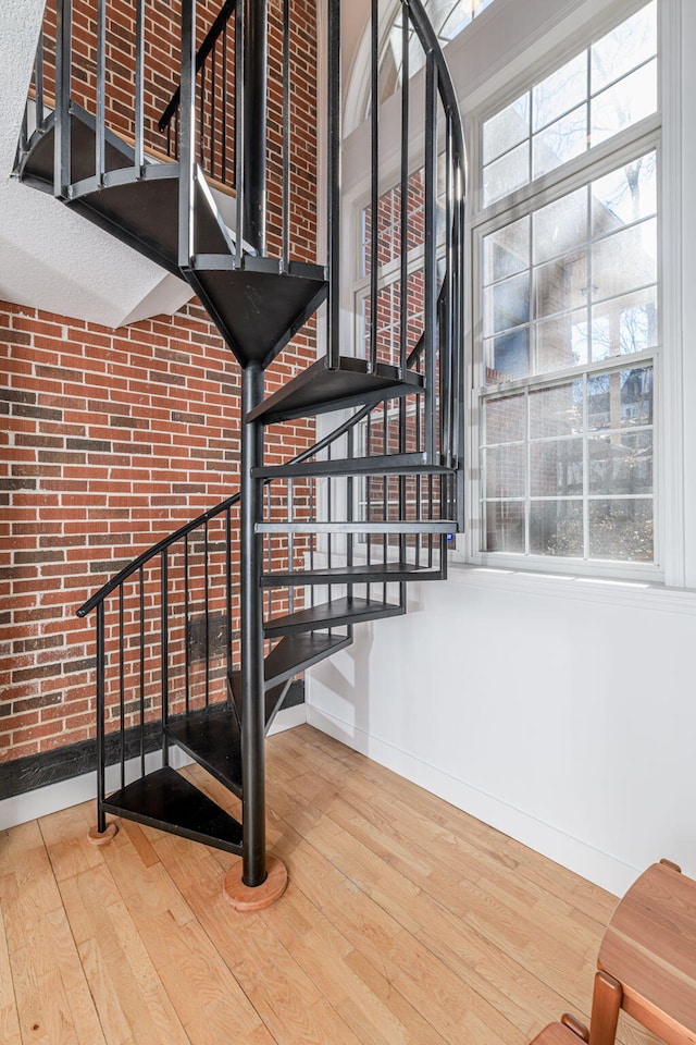 stairs featuring brick wall, wood finished floors, and baseboards