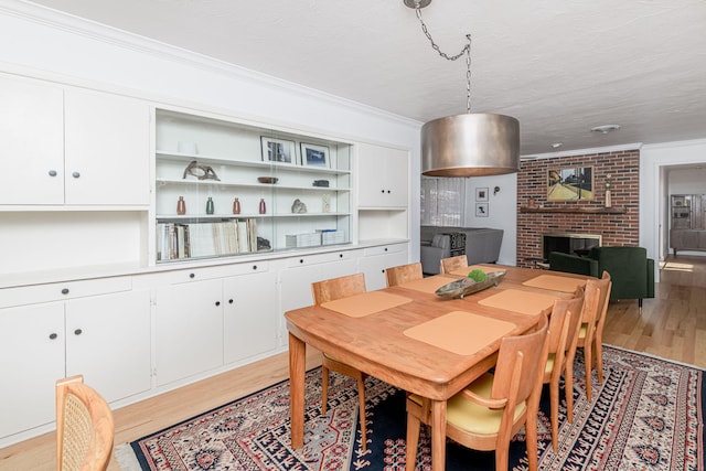 dining space featuring ornamental molding, light wood-style floors, and a fireplace