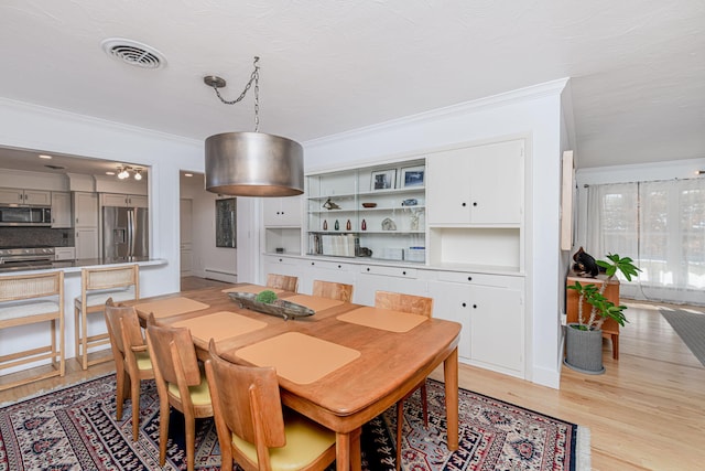 dining space with light wood-style flooring, visible vents, a baseboard radiator, and crown molding