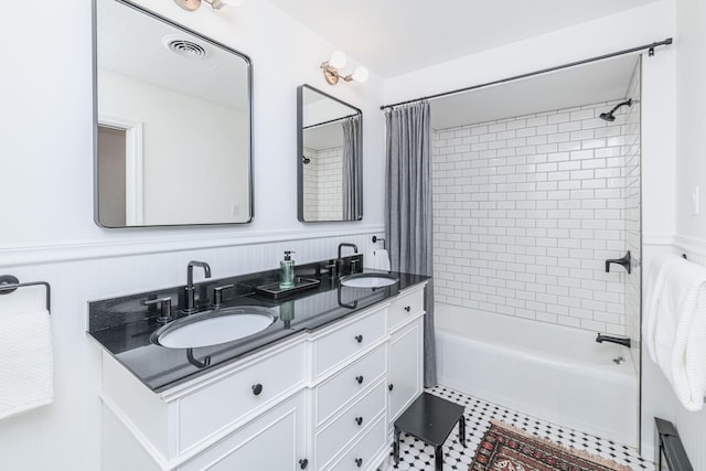 bathroom featuring double vanity, shower / bath combo with shower curtain, wainscoting, and a sink