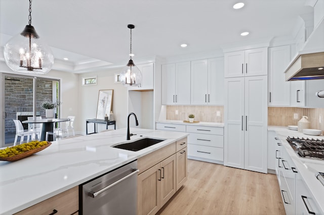 kitchen featuring appliances with stainless steel finishes, light wood-type flooring, a sink, premium range hood, and a notable chandelier