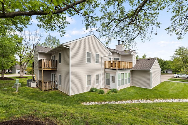 rear view of property featuring a chimney, central AC, a balcony, a yard, and a shingled roof
