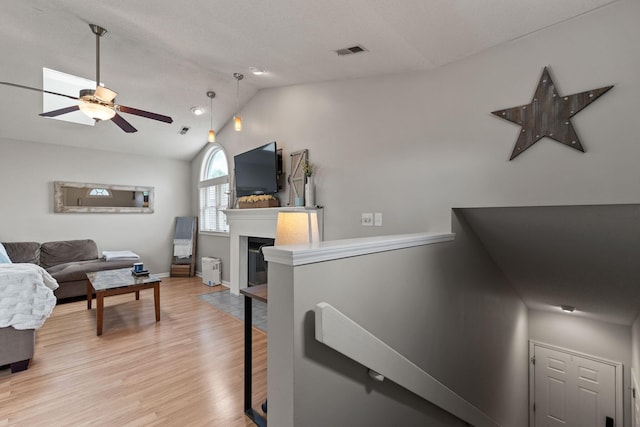 living area featuring ceiling fan, a fireplace, light wood-style flooring, lofted ceiling, and visible vents