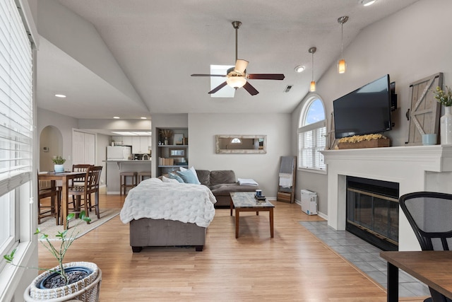 living area featuring light wood-style floors, a fireplace with flush hearth, ceiling fan, and vaulted ceiling
