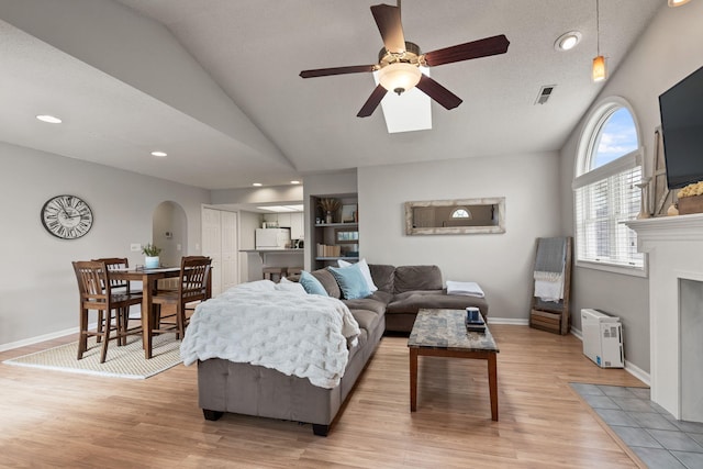 living room featuring visible vents, arched walkways, a ceiling fan, light wood-type flooring, and vaulted ceiling
