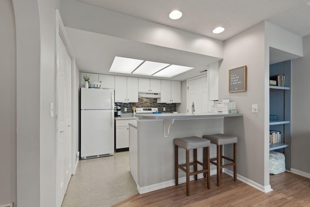 kitchen featuring white cabinets, a kitchen breakfast bar, stove, freestanding refrigerator, and under cabinet range hood