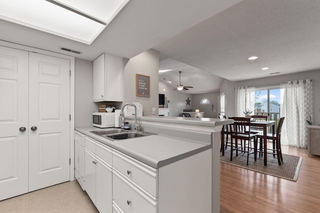 kitchen with a peninsula, ceiling fan, white microwave, white cabinetry, and a sink