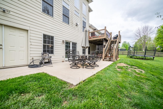 rear view of property featuring a trampoline, a yard, stairway, fence, and a patio area
