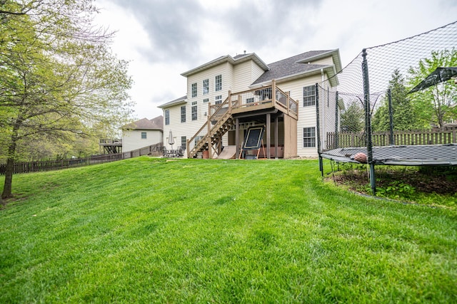 rear view of property with a deck, a trampoline, stairway, and a fenced backyard