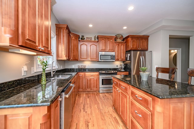 kitchen featuring recessed lighting, dark stone counters, appliances with stainless steel finishes, a sink, and light wood-type flooring
