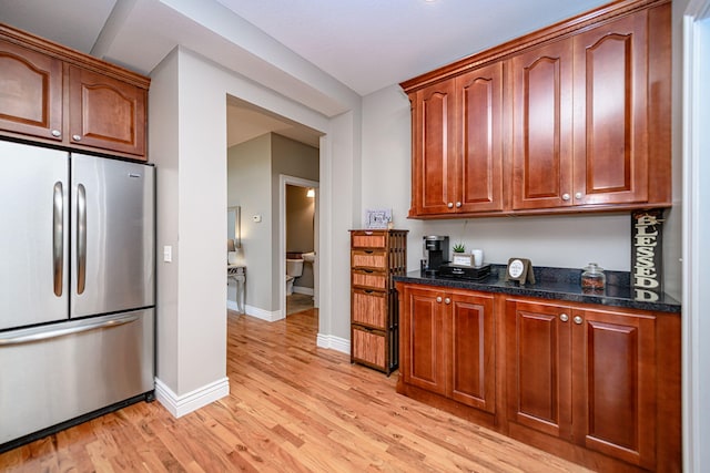 kitchen with light wood finished floors, dark stone countertops, baseboards, and stainless steel refrigerator