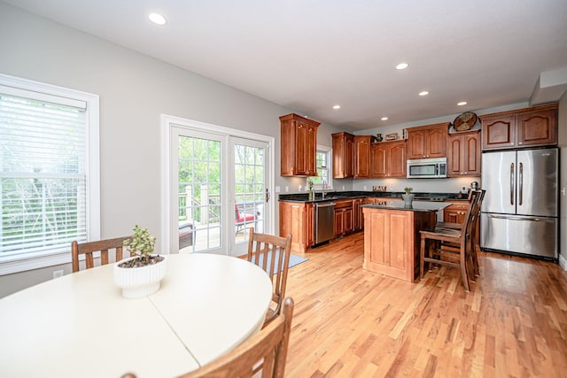 kitchen with recessed lighting, appliances with stainless steel finishes, a kitchen island, dark countertops, and light wood-type flooring