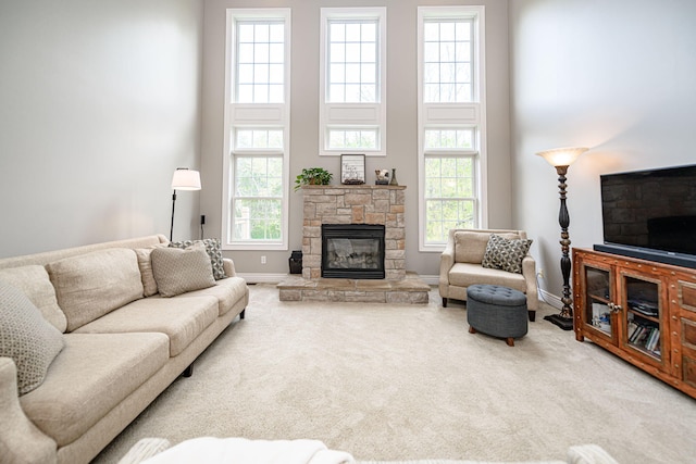 living room featuring carpet flooring, a towering ceiling, a stone fireplace, and a wealth of natural light