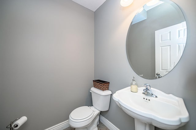 half bath with baseboards, toilet, and a sink