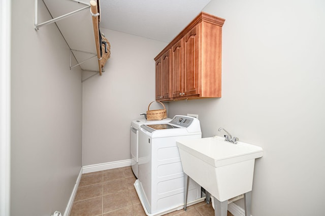 clothes washing area featuring light tile patterned floors, cabinet space, a sink, baseboards, and washer and clothes dryer