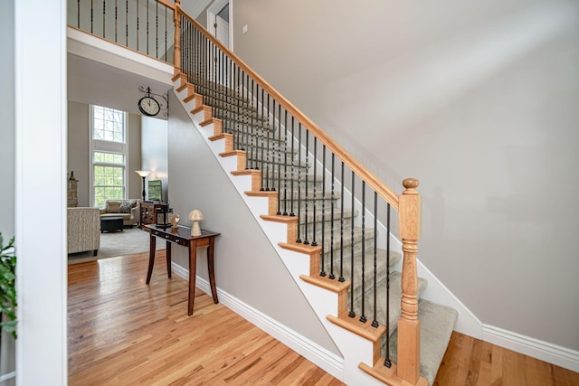 stairway featuring a towering ceiling, wood finished floors, and baseboards