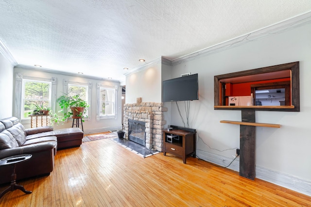 living room featuring a textured ceiling, baseboards, a stone fireplace, ornamental molding, and wood-type flooring