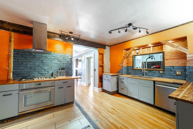 kitchen featuring a sink, butcher block countertops, island range hood, track lighting, and appliances with stainless steel finishes