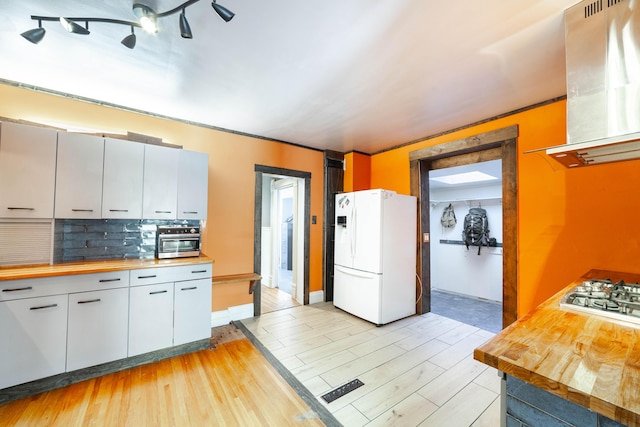 kitchen featuring extractor fan, butcher block counters, decorative backsplash, stainless steel gas cooktop, and white refrigerator with ice dispenser