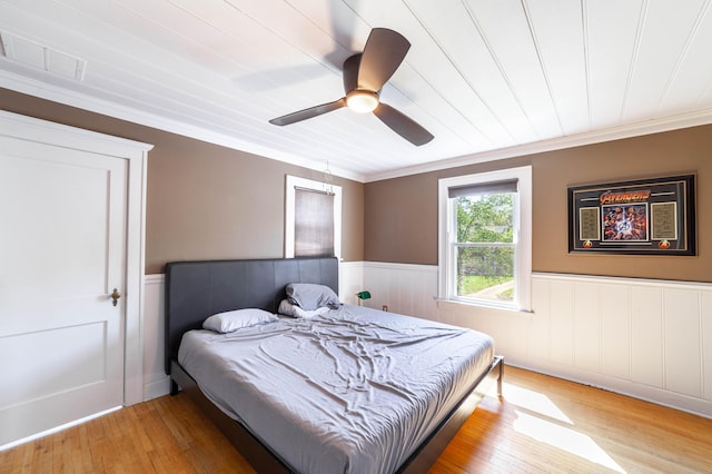 bedroom with a ceiling fan, crown molding, a wainscoted wall, light wood finished floors, and visible vents