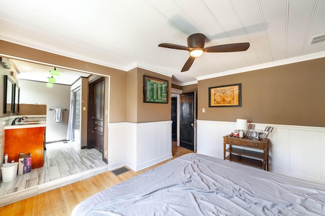 bedroom with wood finished floors, visible vents, ornamental molding, and wainscoting