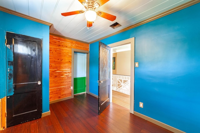unfurnished bedroom featuring a ceiling fan, wood walls, wood finished floors, baseboards, and ornamental molding