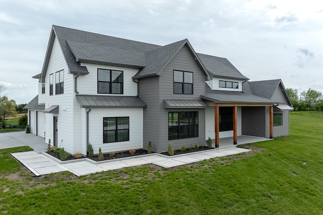modern farmhouse featuring a standing seam roof, a front yard, roof with shingles, concrete driveway, and an attached garage