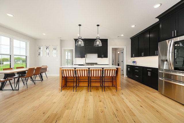 kitchen with dark cabinets, light wood-style floors, a healthy amount of sunlight, light countertops, and stainless steel fridge with ice dispenser