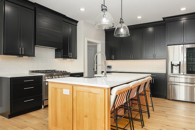 kitchen featuring dark cabinetry, stainless steel appliances, light wood finished floors, and a sink