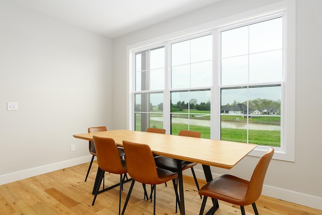 dining space with a water view, light wood-style floors, and baseboards