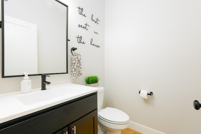 half bathroom featuring toilet, wood finished floors, vanity, and baseboards