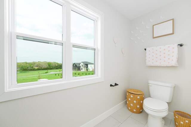 half bathroom with toilet, a wealth of natural light, tile patterned floors, and baseboards