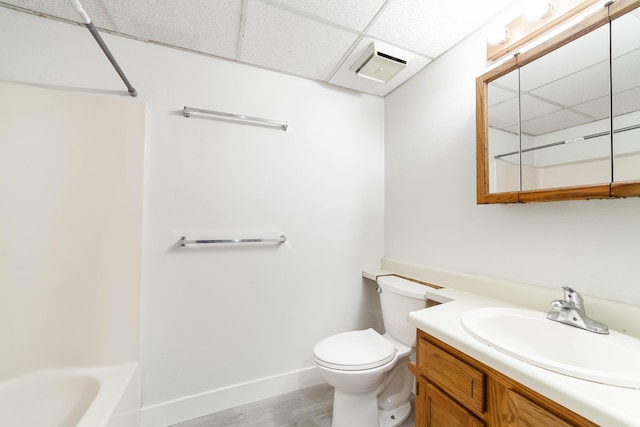 bathroom with wood finished floors, vanity, a drop ceiling, toilet, and visible vents