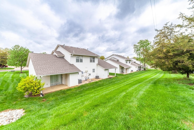 rear view of property featuring a yard, roof with shingles, and a patio area