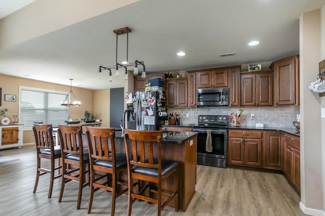 kitchen featuring decorative backsplash, light wood-style flooring, appliances with stainless steel finishes, a breakfast bar, and a center island with sink