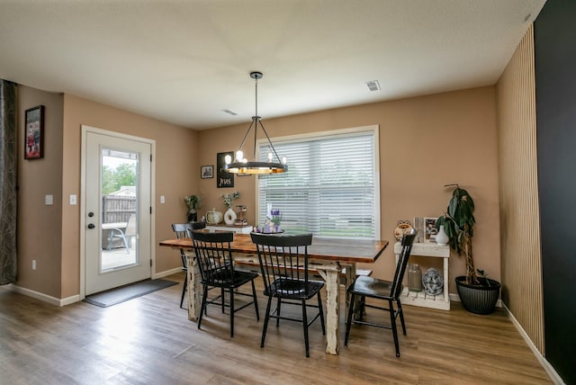 dining space featuring wood finished floors, visible vents, a chandelier, and baseboards