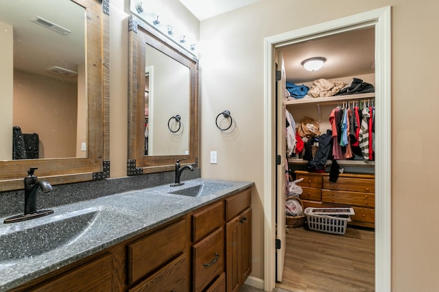 full bath featuring a walk in closet, visible vents, wood finished floors, and a sink