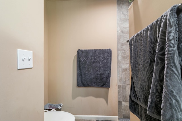 bathroom featuring toilet, a shower, and baseboards