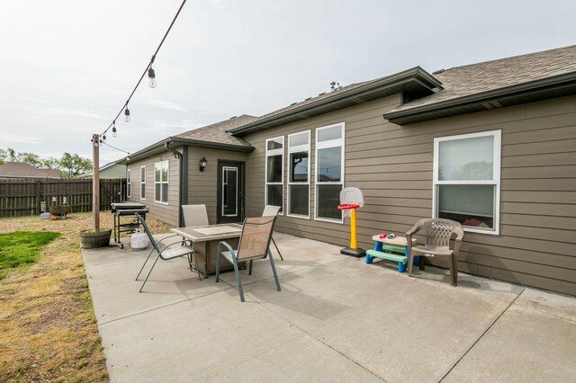 rear view of property with fence, a shingled roof, a patio, and outdoor dining area
