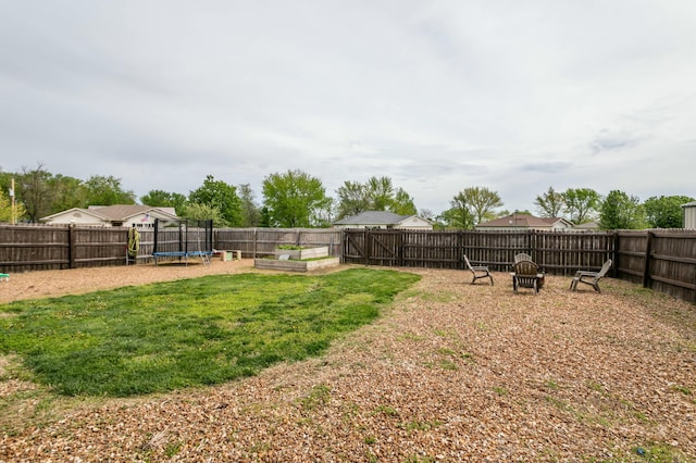 view of yard featuring a fenced backyard, a garden, an outdoor fire pit, and a trampoline
