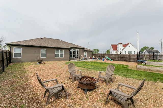 rear view of property featuring a fenced backyard, a playground, an outdoor fire pit, and a trampoline