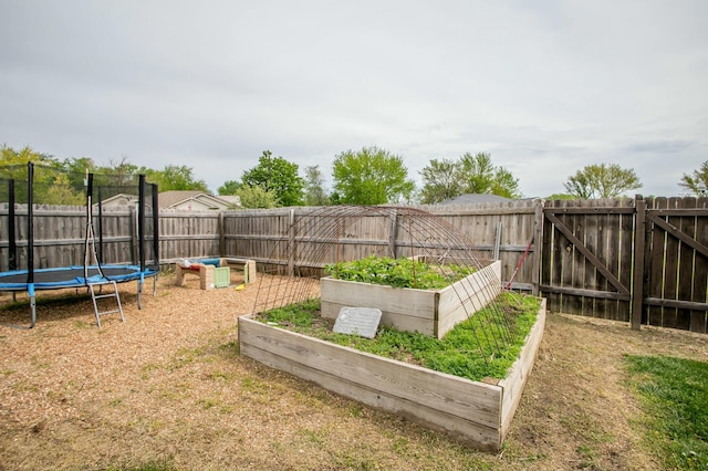 view of yard with a trampoline, a fenced backyard, and a garden
