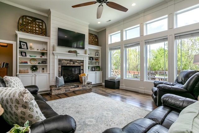 living room with ornamental molding, ceiling fan, a stone fireplace, and hardwood / wood-style flooring
