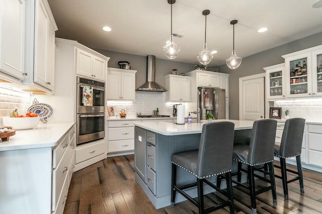 kitchen featuring backsplash, white cabinets, appliances with stainless steel finishes, and wall chimney range hood