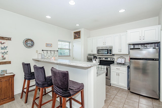 kitchen featuring white cabinets, a breakfast bar area, stainless steel appliances, recessed lighting, and a peninsula